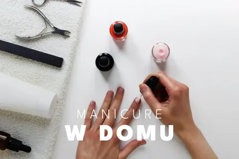 Dłoń malująca paznokcie lakierem, obok buteleczki z lakierami i akcesoria do manicure.