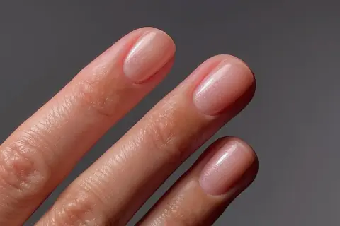 Zbliżenie na dłonie z eleganckimi, różowymi paznokciami z subtelnym połyskiem.