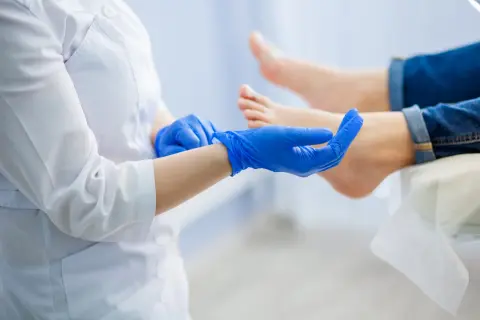 Lekarz w niebieskich rękawiczkach bada stopę pacjenta.