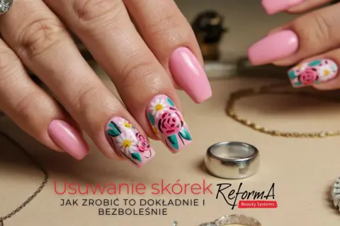 Dłoń z różowymi paznokciami ozdobionymi kwiatowym wzorem, obok biżuteria.