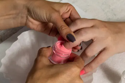 Dłoń zanurza paznokieć w różowym pudrze do manicure tytanowego.